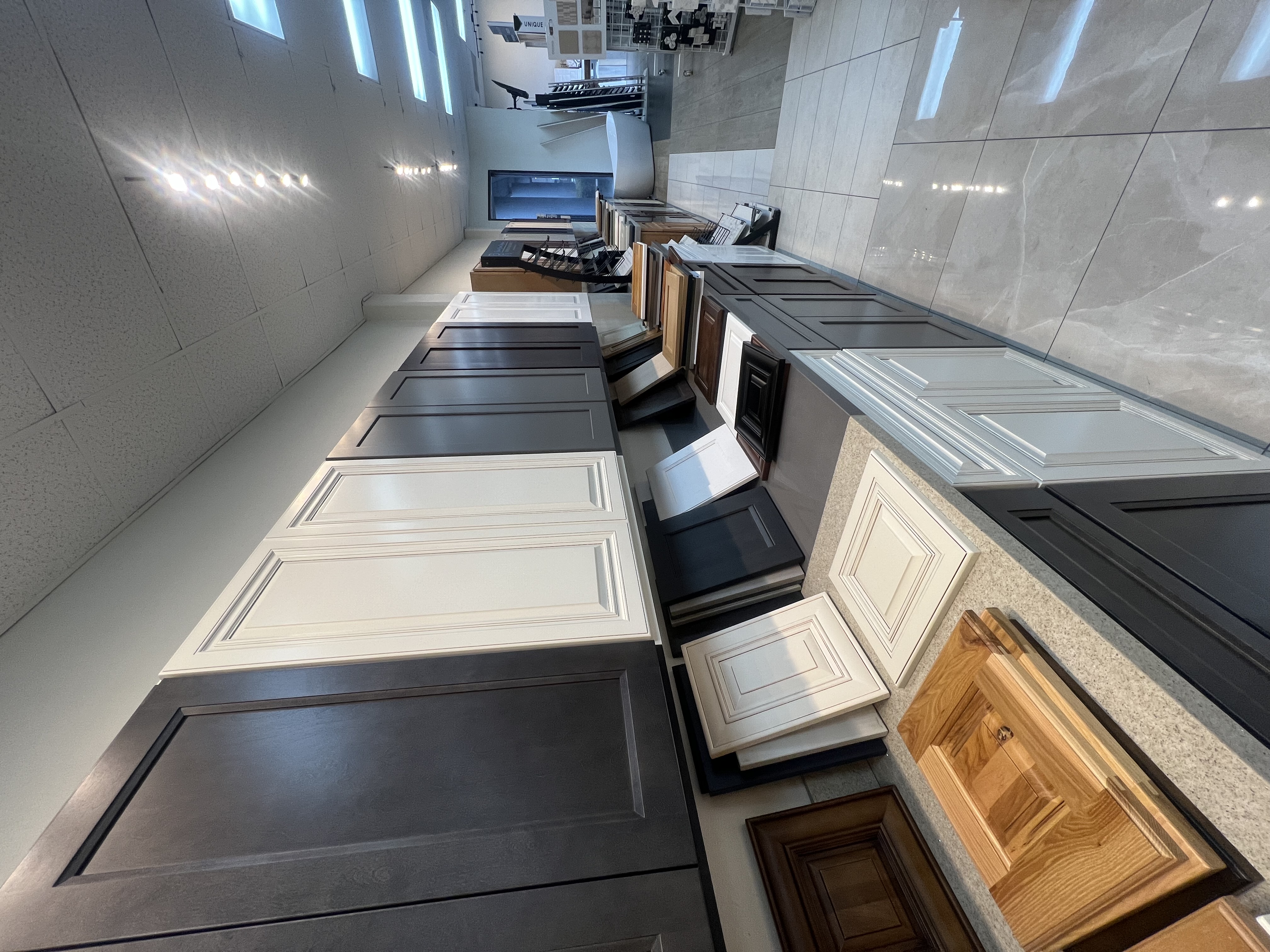 Cabinet door samples in dark, white, and wood finishes displayed along a kitchen and bath showroom wall